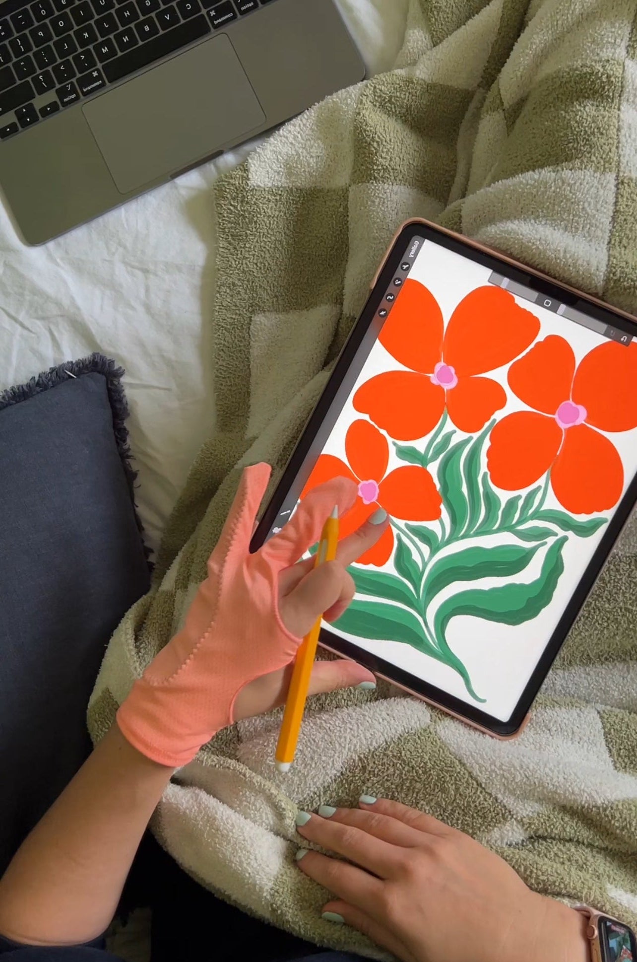Person using a stylus to draw flowers on a tablet with a laptop in the background.