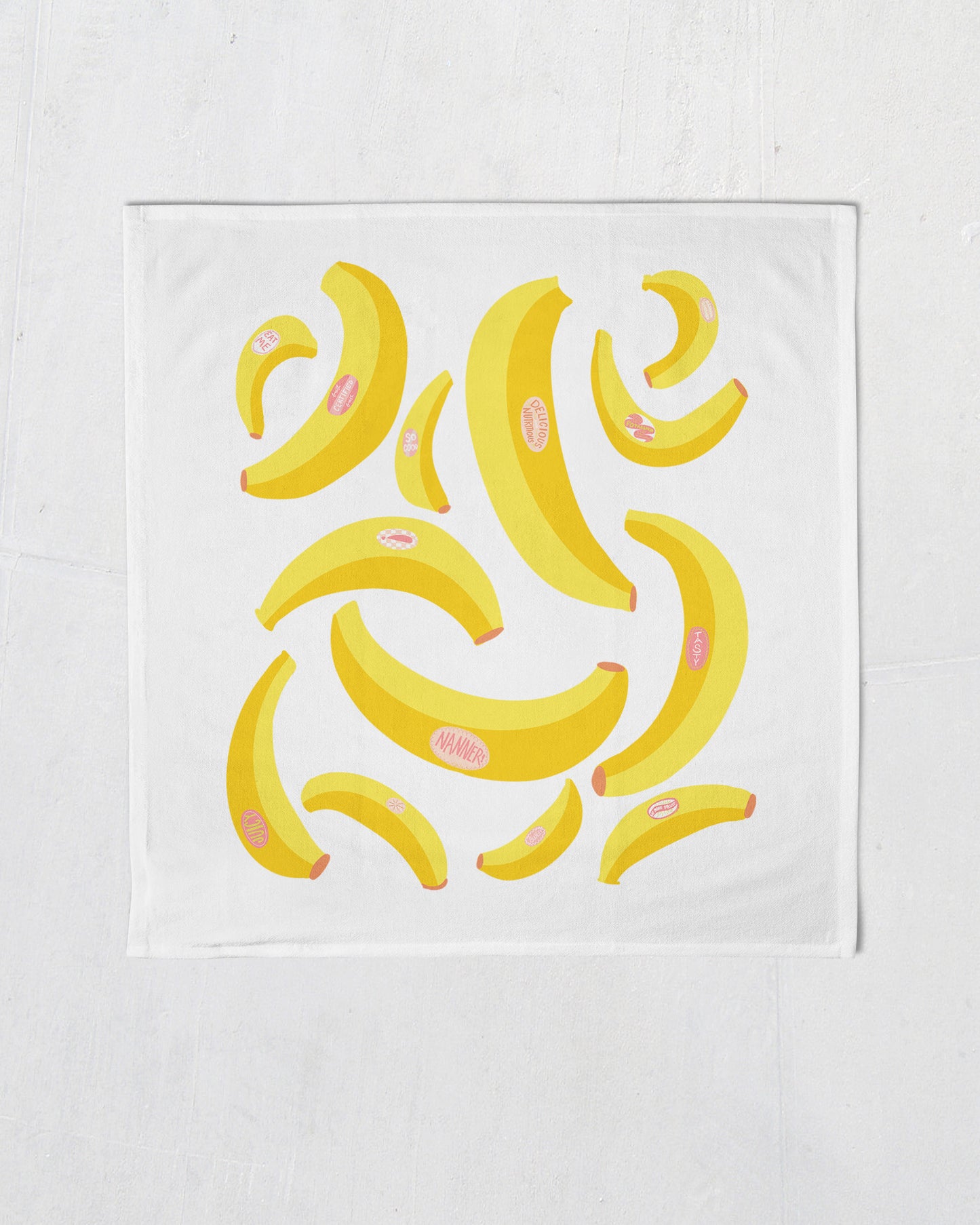 white tea towel with bright yellow bananas with pink fruit stickers printed on it